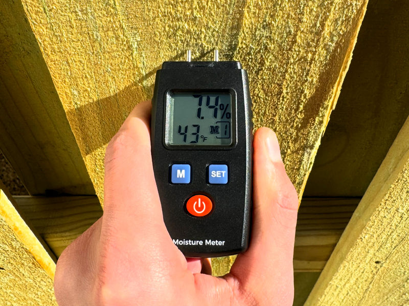 Checking fence wood moisture content with a meter before staining